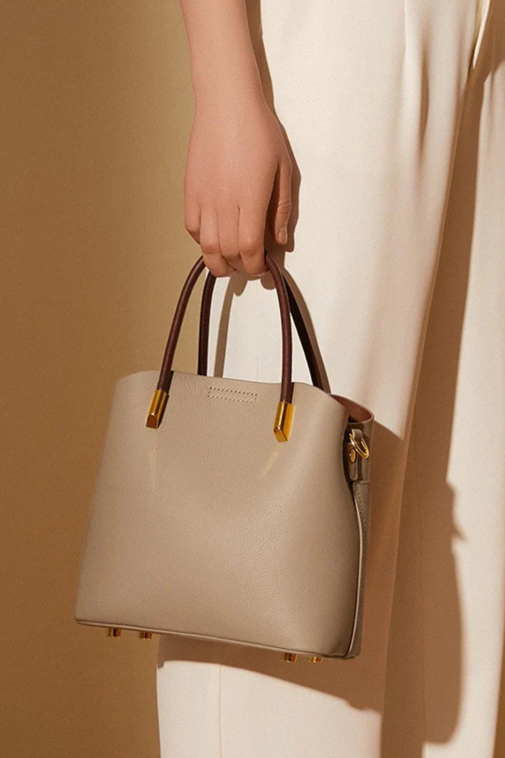 Beige handbag held by a person against a beige background