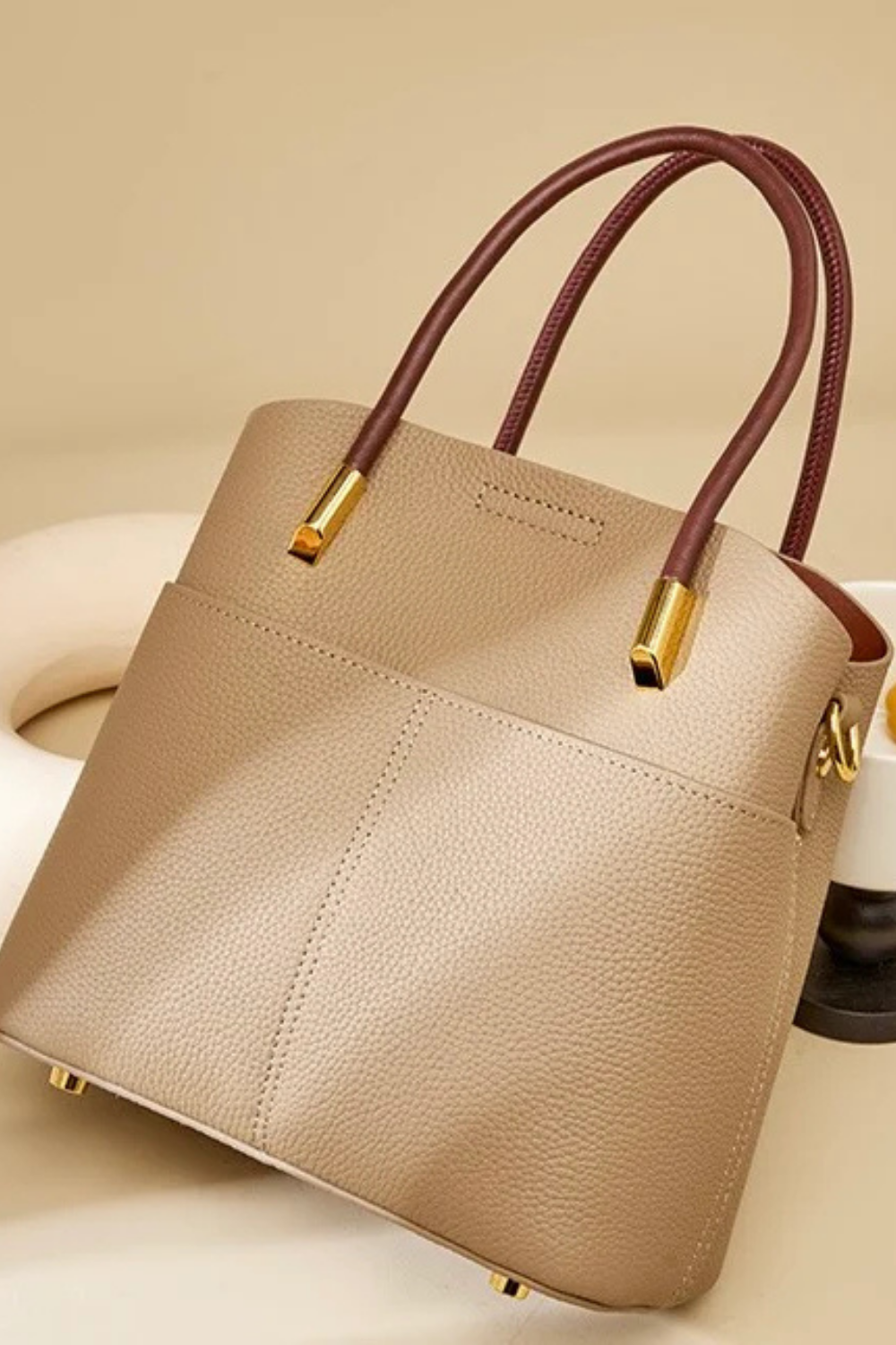 Beige handbag with brown handles on a beige background