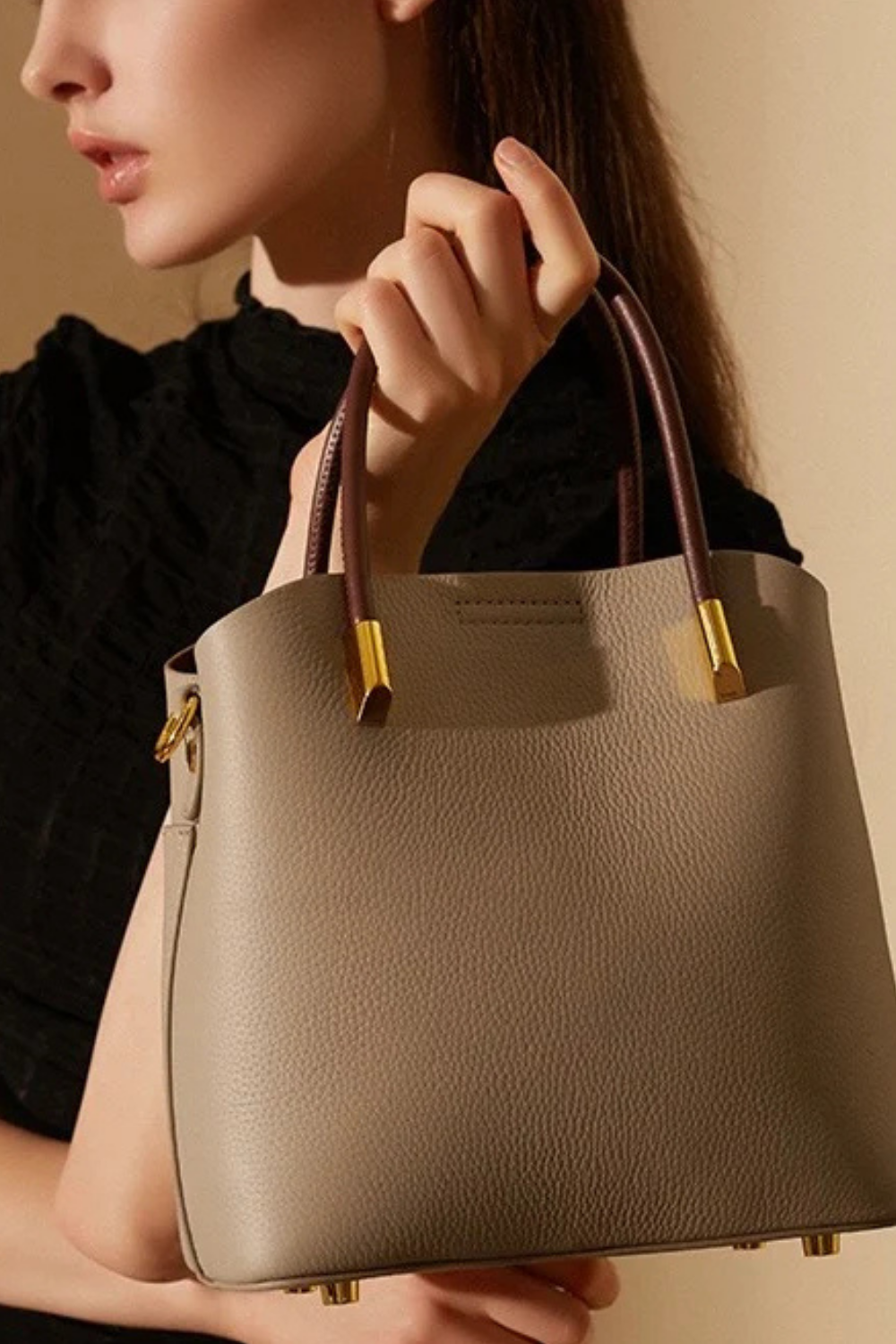 Beige handbag held by a person against a neutral background