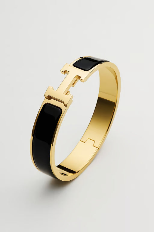 Gold bracelet with black accents on a light gray background