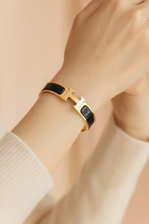 Gold and black bracelet on a wrist against a beige background